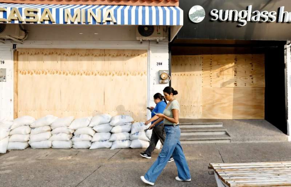 Two women walk past a business boarded up with wooden planks to protect it from the potential impact of Hurricane Simon in Puerto Vallarta, Jalisco state, Mexico. Two women walk past a business boarded up with wooden planks to protect it from the potential impact of Hurricane Simon in Puerto Vallarta, Jalisco state, Mexico